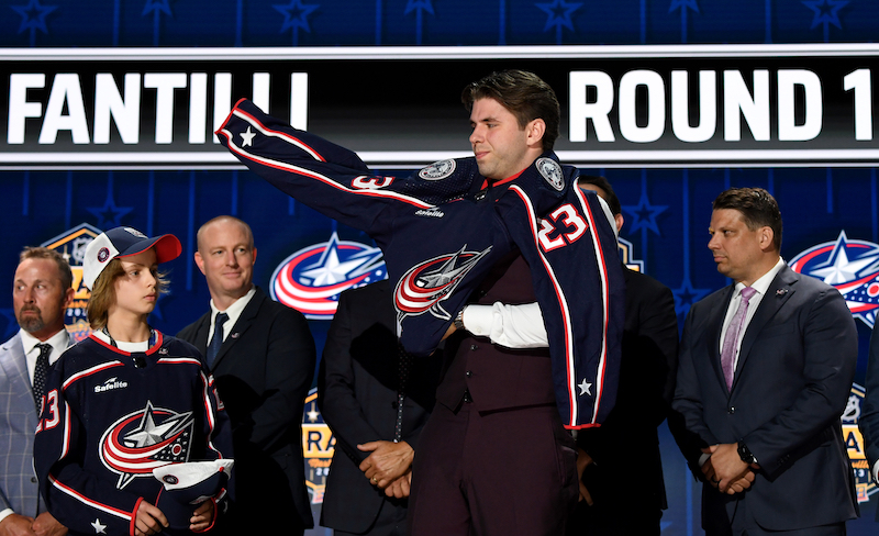 Columbus Blue Jackets draft pick Adam Fantilli puts on his sweater after being selected with the third pick in round one of the 2023 NHL Draft at Bridgestone Arena.