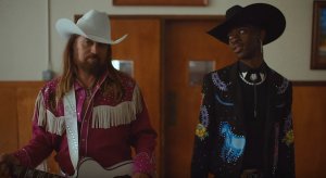Lil Nas X and Billy Ray Cyrus walk into a town hall during their music video for "Old Town Road"