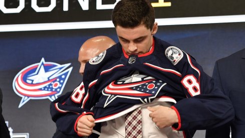 Liam Foudy puts on his jersey after being drafted in the first round by the Blue Jackets