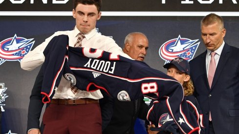 Liam Foudy puts on a team jersey after being selected as the number eighteen overall pick to the Columbus Blue Jackets in the first round of the 2018 NHL Draft at American Airlines Center. 