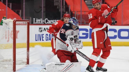Jan 19, 2021; Detroit, Michigan, USA; Columbus Blue Jackets goaltender Elvis Merzlikins (90) makes a save as Detroit Red Wings left wing Mathias Brome (86) watches during the second period at Little Caesars Arena.