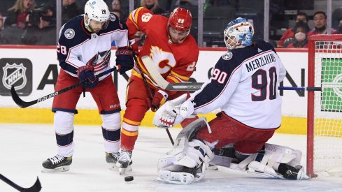 Feb 15, 2022; Calgary, Alberta, CAN; Calgary Flames forward Dillon Dube (29) battles for the puck with Columbus Blue Jackets forward Oliver Bjorkstrand (28) and goalie Elvis Merzlikins (90) during the first period at Scotiabank Saddledome.