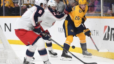 Nashville Predators center Philip Tomasino handles the puck behind the net against Columbus Blue Jackets defenseman Adam Boqvist and Columbus Blue Jackets defenseman Zach Werenski during a hotly contested game.