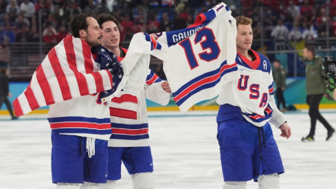 Feb 22, 2026; Milan, Italy; Auston Matthews (34) of the United States, Zach Werenski (8) of the United States and Matthew Tkachuk (19) of the United States hold up the jersey of John Gaudreau after defeating Canada in the men's ice hockey gold medal game during the Milano Cortina 2026 Olympic Winter Games at Milano Santagiulia Ice Hockey Arena.