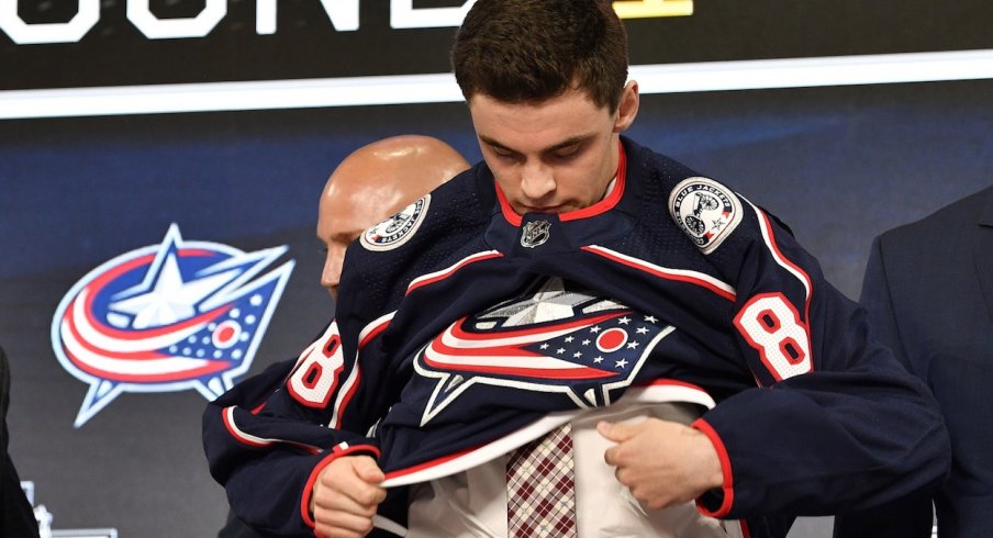 Liam Foudy puts on his jersey after being drafted in the first round by the Blue Jackets