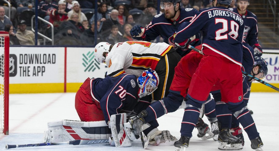 Nov 2, 2019; Columbus, OH, USA; Columbus Blue Jackets goaltender Joonas Korpisalo (70) covers the puck while Calgary Flames left wing Matthew Tkachuk (19) falls on him during the game at Nationwide Arena. Mandatory Credit: Jason Mowry-USA TODAY Sports