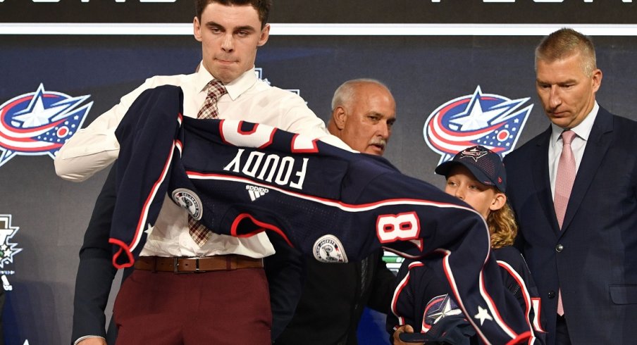 Liam Foudy puts on a team jersey after being selected as the number eighteen overall pick to the Columbus Blue Jackets in the first round of the 2018 NHL Draft at American Airlines Center. 