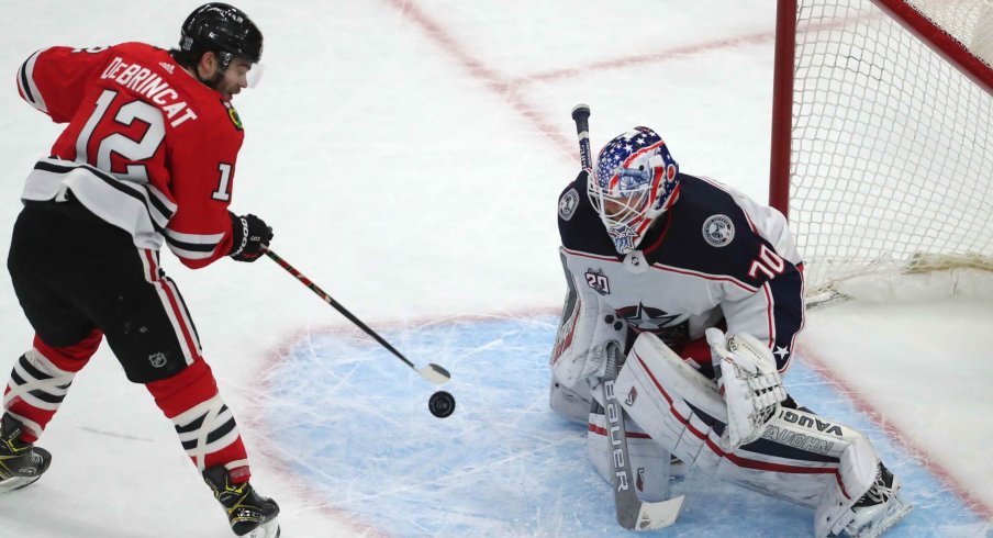 Feb 13, 2021; Chicago, Illinois, USA; Chicago Blackhawks left wing Alex DeBrincat (12) scores the game winning goal against Columbus Blue Jackets goaltender Joonas Korpisalo (70) during the overtime period at the United Center. Chicago won 3-2.