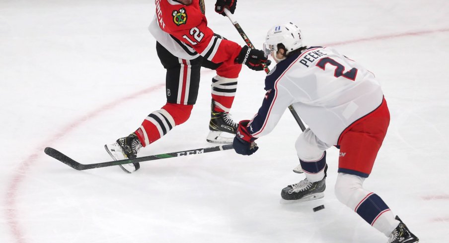 Feb 13, 2021; Chicago, Illinois, USA; Chicago Blackhawks left wing Alex DeBrincat (12) shoots between the legs of Columbus Blue Jackets defenseman Andrew Peeke (2) during the second period at the United Center.