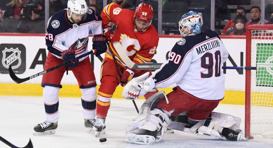 Feb 15, 2022; Calgary, Alberta, CAN; Calgary Flames forward Dillon Dube (29) battles for the puck with Columbus Blue Jackets forward Oliver Bjorkstrand (28) and goalie Elvis Merzlikins (90) during the first period at Scotiabank Saddledome.