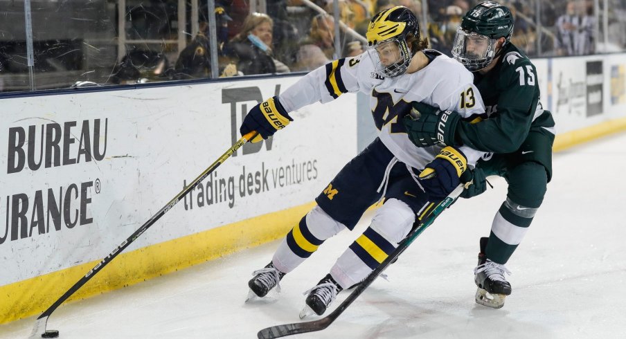 Michigan forward Kent Johnson (13) is defended by Michigan State defenseman Christian Krygier (15) during the first period of the first game in their Big Ten quarterfinal matchup at Yost Ice Arena in Ann Arbor on Friday, March 4, 2022.