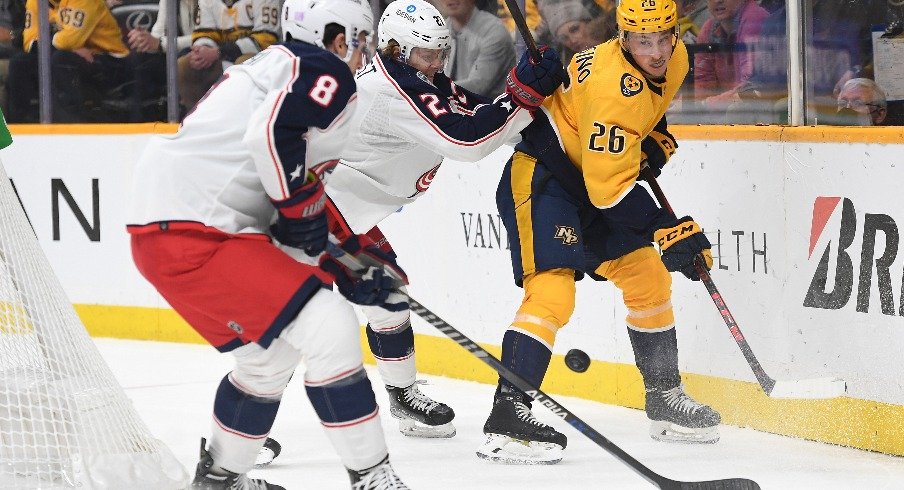 Nashville Predators center Philip Tomasino handles the puck behind the net against Columbus Blue Jackets defenseman Adam Boqvist and Columbus Blue Jackets defenseman Zach Werenski during a hotly contested game.