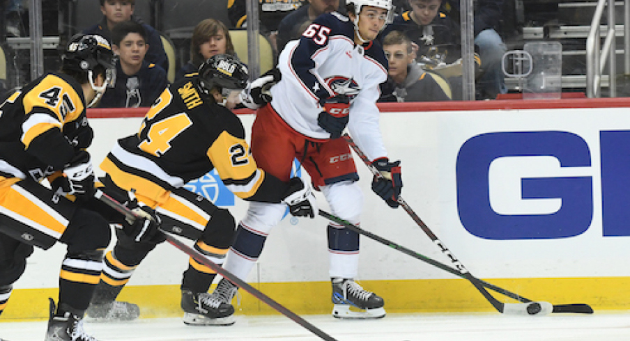 Columbus Blue Jackets center Luca Del Bel Belluz (65) moves the puck away from Pittsburgh Penguins defenseman Ty Smith (24) and forward Jonathan Gruden (45) during the first period at PPG Paints Arena.