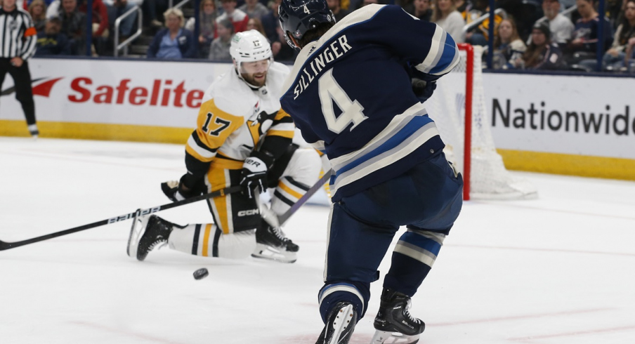 Columbus Blue Jackets forward Cole Sillinger shoots as Bryan Rust drops to block 