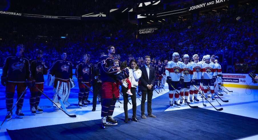 Columbus Blue Jackets center Sean Monahan (23) holds Johnny Gaudreau’s child along side Meredith Gaudreau and family as a banner is raised in honor of Johnny before the home opener at Nationwide Arena.